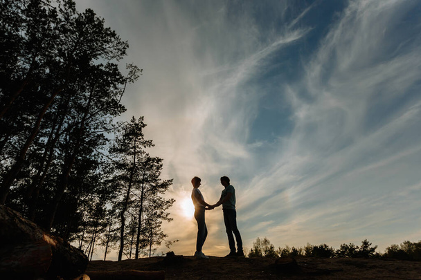 Silhouette of a girl and a guy holding hands against the background of the sunset - Foto, Imagem
