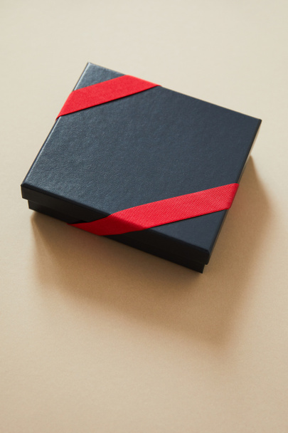 black gift box with red ribbon on beige background  - 写真・画像