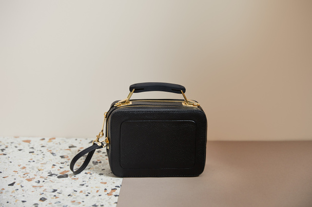 Кожа черная сумка с золотыми молниями на мраморной поверхности на бежевом фоне
 - Фото, изображение