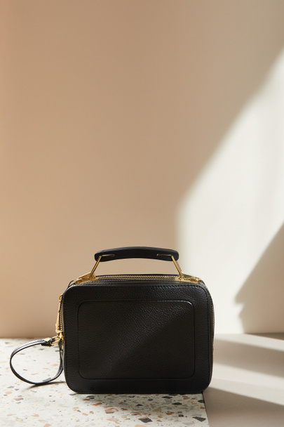 leather black handbag with golden zippers on marble surface on beige background - Foto, Imagem