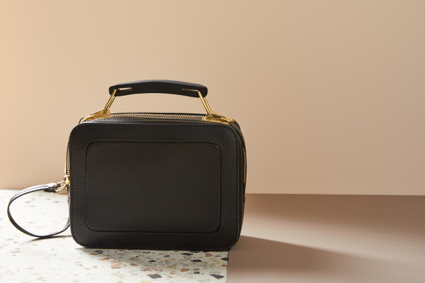 leather black handbag with golden zippers on marble surface on beige background - Foto, imagen