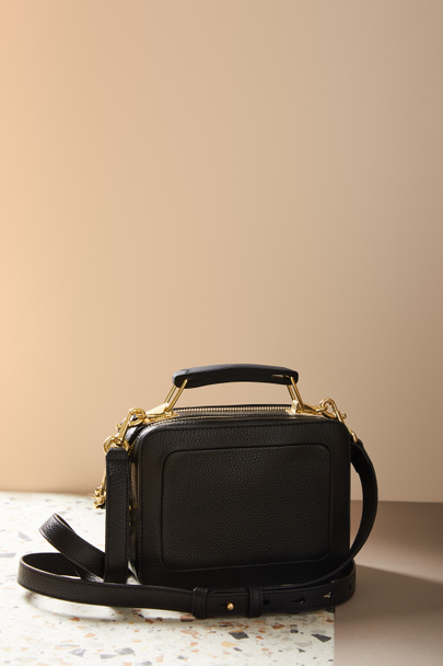 leather black handbag with golden zippers on marble surface on beige background - Foto, Bild