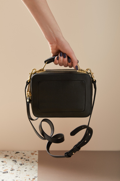 przycięty widok kobiety trzymającej skórzaną czarną torebkę ze złotymi zamkami na beżu - Zdjęcie, obraz