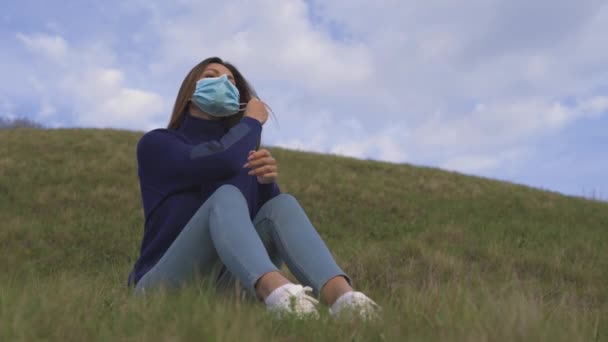 De jonge vrouw zit op het groene gras en neemt haar medische masker af - Video