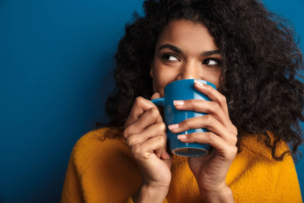 Image of a pretty young african woman posing isolated over blue wall background drinking tea. - Fotoğraf, Görsel
