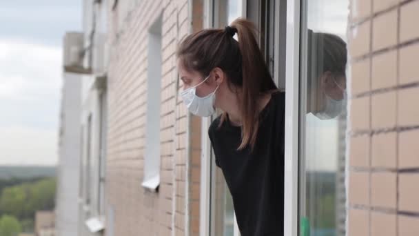 woman in a medical mask looks out of an open window during isolation - Záběry, video