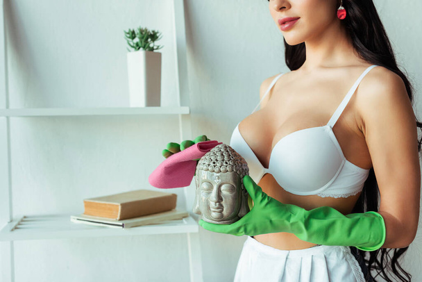 Обрізаний вид сексуальної дівчини в бюстгальтер і гумові рукавички очищення декоративної статуетки вдома
  - Фото, зображення