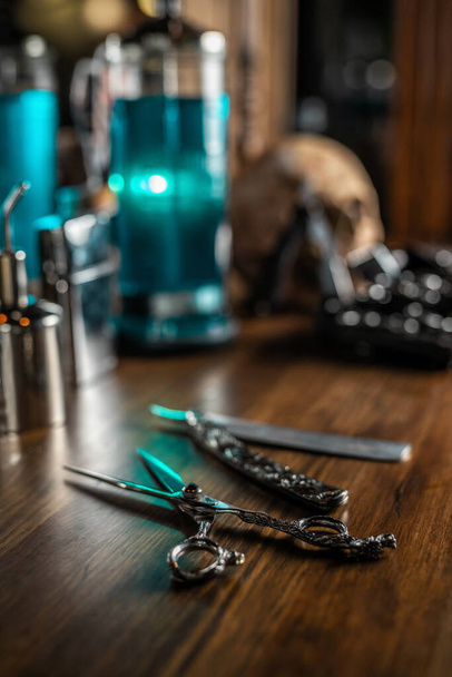 Zestaw nożyczek, ostrzy i innych akcesoriów do fryzjera na starym brązowym drewnianym stole, z rozmytym tłem - Zdjęcie, obraz