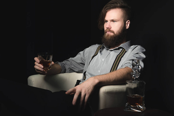 Portrait of a pensive handsome young man, with a glass of alcohol in his hands, on an isolated black background. The concept of pastime, rest and relaxation - Fotoğraf, Görsel