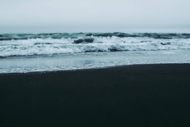 Rozmazané pozadí. Modrobílé vlny oceánu šplouchající po černém písečném pobřeží na Islandu - Fotografie, Obrázek