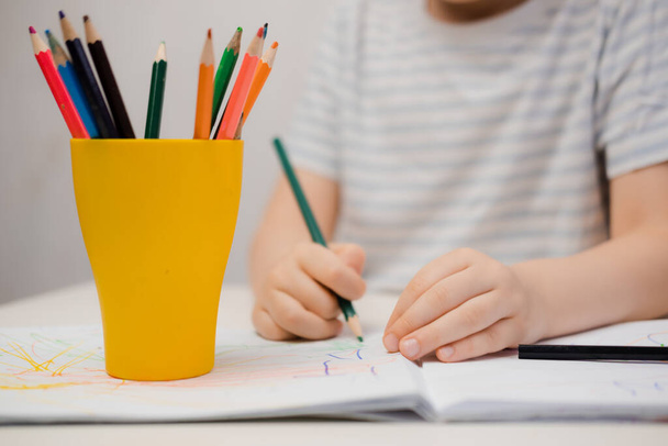 Egy kisfiú ül az asztalnál, és színes ceruzákkal rajzol. - Fotó, kép