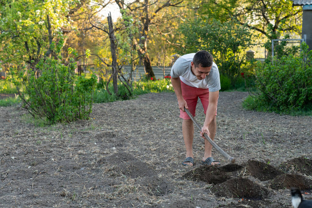 Nuori rento mies työskentelee kuokan kanssa maaperässä
 - Valokuva, kuva
