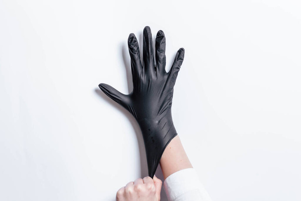 Main en gants noirs d'un médecin ou d'un coiffeur sur fond blanc. Des gants sont portés sur la main. La fille met un gant noir sur sa main. mitaine noire sur sa main
. - Photo, image