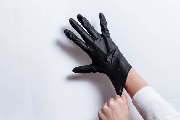 Hand in zwarte handschoenen van een arts of kapper op een witte achtergrond. Handschoenen worden op de hand gedragen. Het meisje doet een zwarte handschoen om haar hand. Zwarte handschoen op zijn hand. - Foto, afbeelding