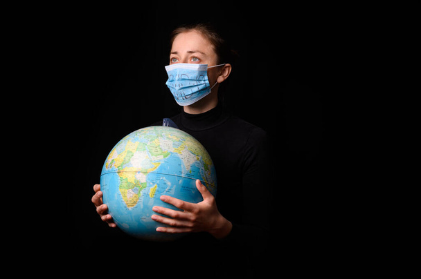 Woman hands holding the Earh globe in the hands. Woman in the doctor breath medicine mask. Coronavirus protection for people all continents and the world. Isolated on a black background. Concept stop covid-19. - Fotografie, Obrázek