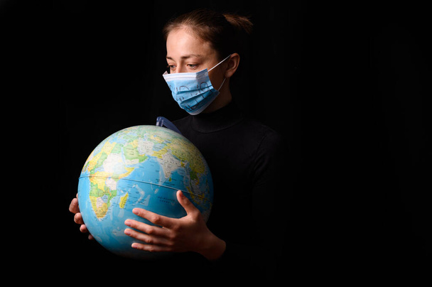 Woman hands holding the Earh globe in the hands. Woman in the doctor breath medicine mask. Coronavirus protection for people all continents and the world. Isolated on a black background. Concept stop covid-19. - Photo, image
