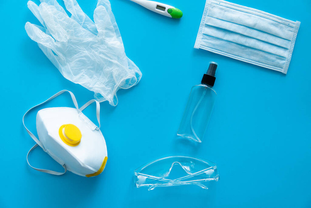 Medical protective mask, respirator ffp, rubber gloves, antiseptic, thermometer and protective glasses lie on a blue background. Anti-virus protection kit against covid-19. Coronavirus pandemic 2019. - Фото, зображення