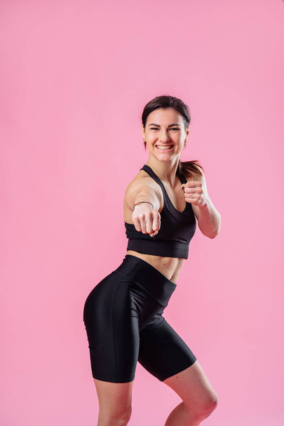 Slim woman is kicking the air, with hand and leg up . Athletic girl doing boxing exercises, making a direct kick. Photo of a young girl isolated on a pink background. Strength and motivation. - Photo, Image