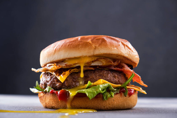 Tasty grilled beef burger with fried bacon and eggs, cheese, tomatoes and lettuce.  - Foto, Imagem