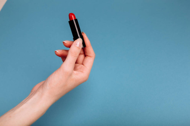 The woman's hand is taking red lipstick. isolated On the blue background. - Foto, immagini