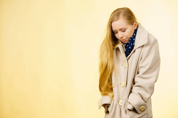 Woman wearing autumnal beige coat feeling cold. Fall overcoats, outfit and fashion concept. Studio shot on yellow background - Φωτογραφία, εικόνα