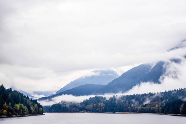 Nebbia e nuvole che coprono le montagne boschive vicino al lago nella Columbia Britannica, Canada
. - Foto, immagini