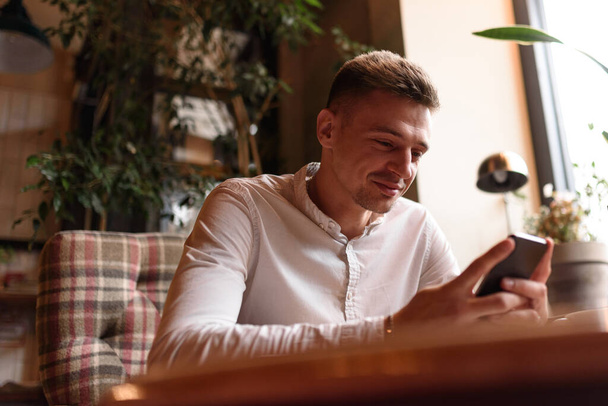 Uśmiechnięty mężczyzna korzystający z telefonu komórkowego w kawiarni - Zdjęcie, obraz