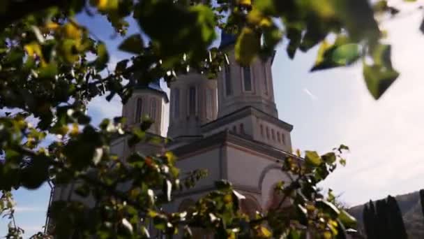 Egy nagy fehér templom három kék kupolával a perzselő nap alatt egy forró nyári napon, panorámás kilátás egy fa zöld levele mögül, széles terv. - Felvétel, videó