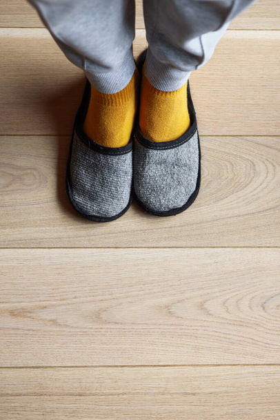 Πόδια σε κίτρινες κάλτσες και μάλλινες παντόφλες σε ξύλινο πάτωμα. - Φωτογραφία, εικόνα