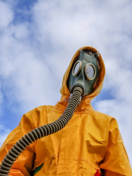 portrait of a human in a gas mask and a protective yellow suit on a background of blue sky. - Valokuva, kuva
