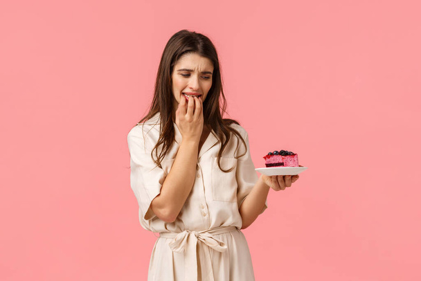 Cant resist temptation. Young woman on diet, trying eat healthy food want take bite of delicious blueberry cake, biting fingernails and staring on plate, standing pink background with desire - Φωτογραφία, εικόνα