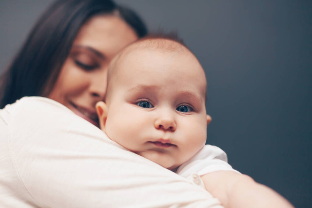 Close-up portrait of a serene beautiful baby boy and happy smiling mother. Baby in hand of mother. Healthcare and medical love woman mothers day concept. - Fotoğraf, Görsel