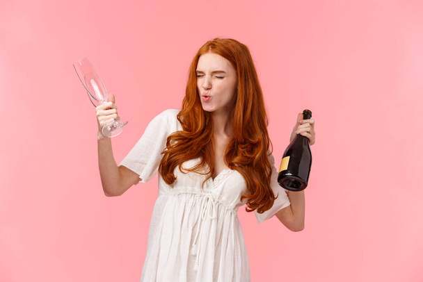 Мбаппе, вечеринка и веселая концепция. Пьяная и беззаботная, взволнованная рыжая женщина, стоящая впустую, чувствующая головокружение и оптимизм, держащая бутылку шампанского и бокал, похмелье рядом
 - Фото, изображение