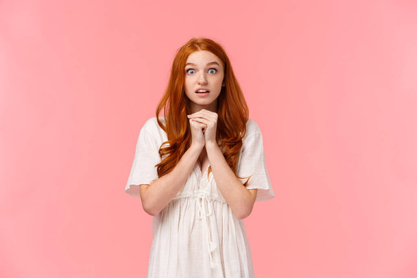 Hopeful and amused, redhead female in white dress, holding hands together over chest in praying pose, glancing camera nervously anticipate important news, seeing something heartwarming - Photo, Image