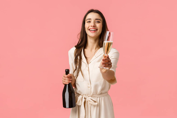 Tady máš. Romantický něžná mladá brunetka žena otevřena láhev šampaňské smích a usmívání dávat sklenici na přítelkyni, navrhnout oslavit zvláštní příležitost společně, růžové pozadí - Fotografie, Obrázek