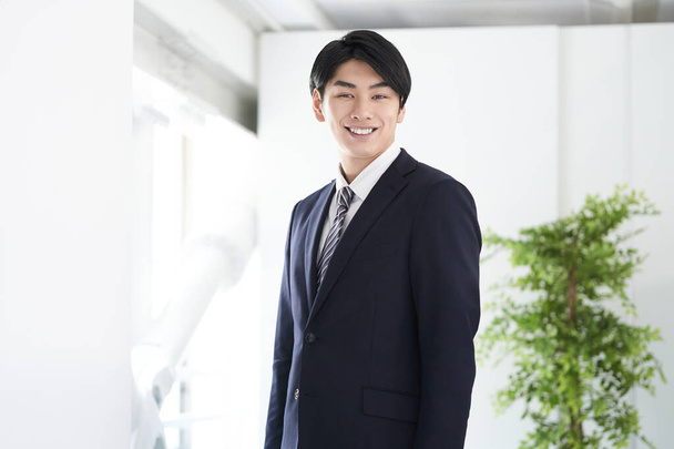 Γιαπωνέζος επιχειρηματίας χαμογελάει και κοιτάζει την κάμερα. - Φωτογραφία, εικόνα
