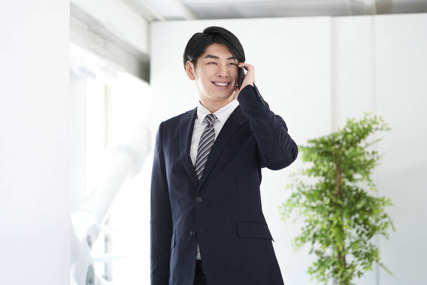 Egy japán férfi üzletember mosollyal az arcán telefonál.. - Fotó, kép