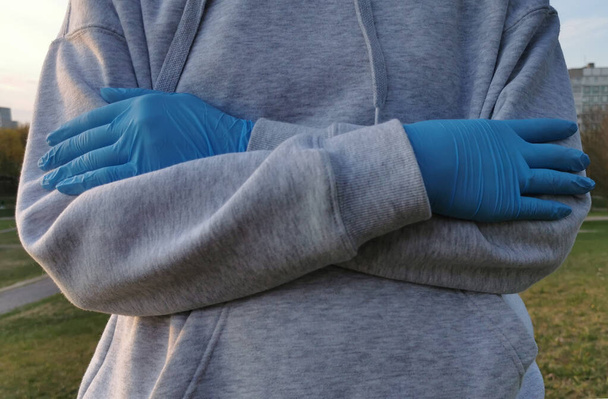 Χέρια ενός κοριτσιού με ιατρικά γάντια στο δρόμο την άνοιξη. Προστασία από τον ιό Coronavirus 2020. - Φωτογραφία, εικόνα