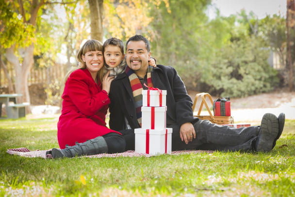 Família de raça mista desfrutando de presentes de Natal no parque juntos
 - Foto, Imagem