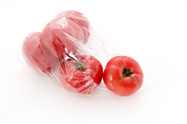 Beyaz zemin üzerinde plastik torba içinde olgun kırmızı domatesler - Fotoğraf, Görsel