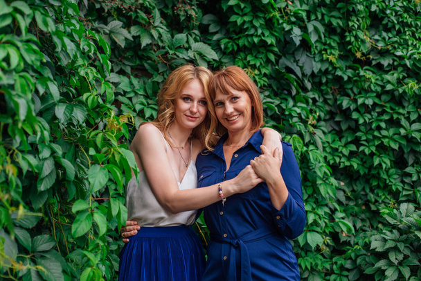 Beautiful mother and her grown up daughter hugging each other on a summer day outside on a green nature background - Photo, image