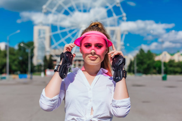 Portrait of an emotional beautiful young girl in a pink cap visor and protective gloves for rollerblades and skateboarding. - Foto, imagen