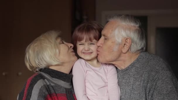 Grandfather and grandmother kissing on cheeks their kid granddaughter at home - Footage, Video
