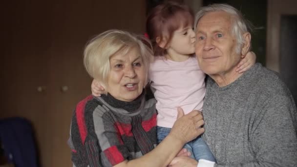 Wnuczka całuje starszego uśmiechniętego dziadka z babcią w domu - Materiał filmowy, wideo
