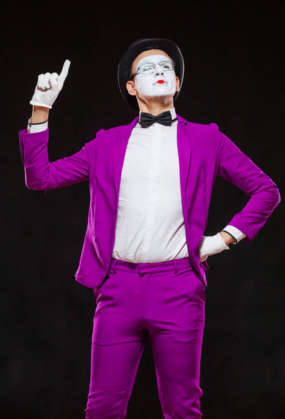Portrait of male mime artist, isolated on black background. Young man in purple suit is standing with risen finger. Symbol of attention, warning, nota bene - Fotografie, Obrázek
