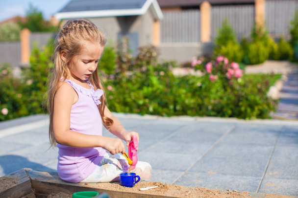 Little cute girl playing at the sandbox with toys in yard - Foto, imagen
