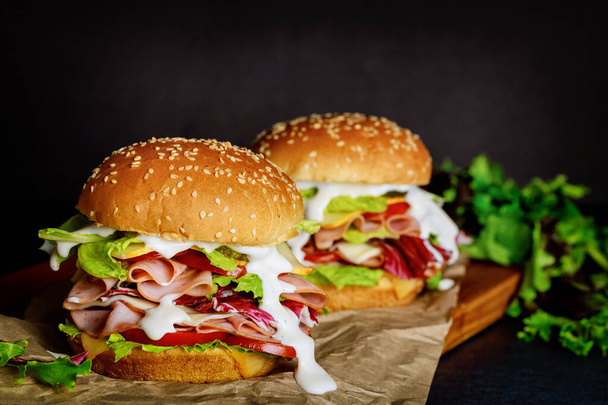 Zwei frische Sandwiches mit Schinken, Käse, Tomaten, Salat auf dunklem Hintergrund. - Foto, Bild