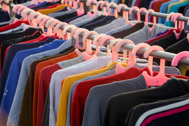Huge selection of different used clothes for men, women and children on the rack in a second hand shop or thrift store. Concept of waste problem in fashion industry. - Photo, Image