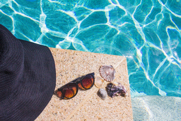 musta hattu, aurinkolasit ja simpukat altaan reunaan
 - Valokuva, kuva