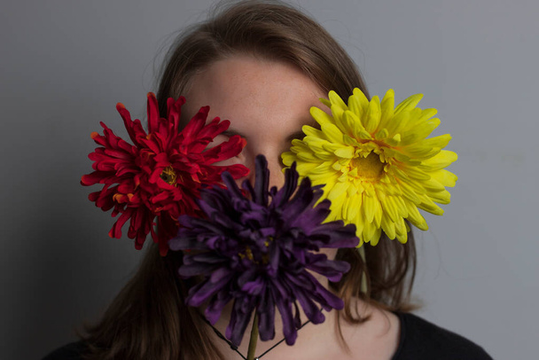 young blonde girl with three red, yellow and purple flowers on her face - Fotoğraf, Görsel